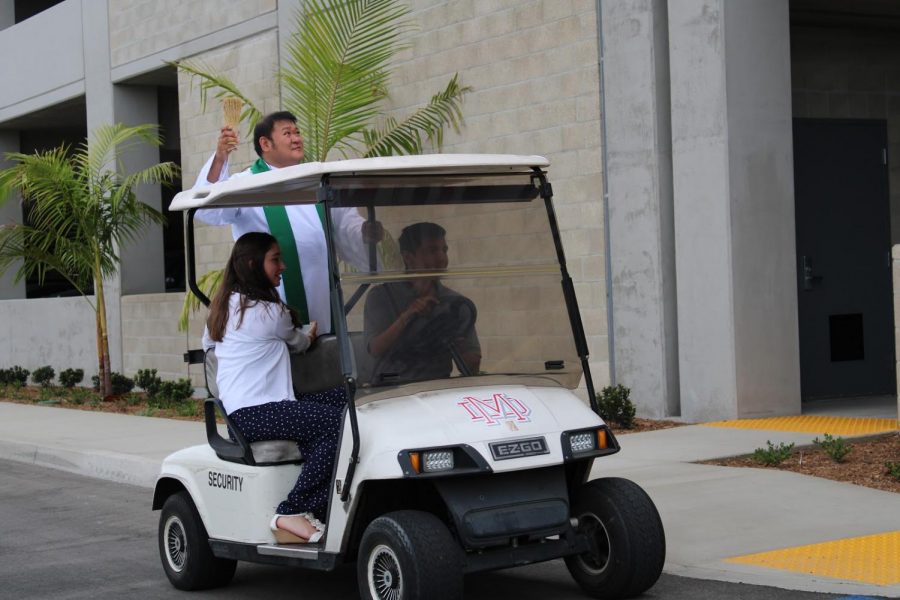 BLESSING IN DISGUISE: Circling the newly built parking structure, Father Mark Cruz blesses the building before Family Mass on Sept. 22 while senior Alizea Hinz holds the bowl of Holy Water for him. The blessing of the structure was live-streamed for families inside of the Meruelo Athletic Center to see. 