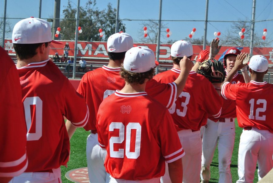 CELEBRATIONS: Senior Brett Nelson is congratulated by his teammates after sliding safely into home plate and scoring a run in the Varsity Red vs. White scrimmage game. The Red and White Day is an annual tradition kicking off baseball season, where all baseball teams play friendly games. The event also included live music, catering, and shopping.