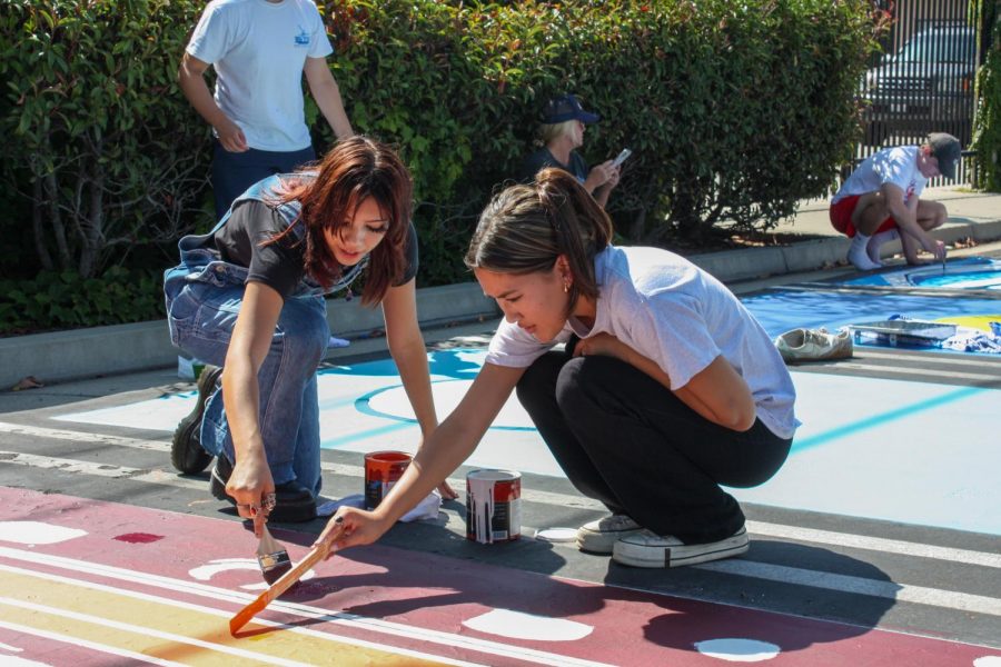 MUSICAL INSPIRATION: Paige Buttaccio (left), a rising senior, paints her reserved parking spot that is inspired by a cassette tape. Buttaccio worked with a friend to make the spot represent both a mixtape and her love of music. “I feel like I always listen to music at school and it gets me through stuff, so I wanted to include it in my spot,” Buttaccio said.