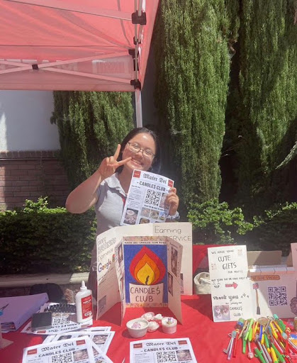 MAKING HER MARK Tran poses at her booth and promotes the Candles Club at the annual Mater Dei club rush in Fall of 2023. As President of the club, Tran takes part in producing candles from wax and making a workshop for other members to sell their candles. The money Tran and her peers fundraise is donated to charity in order to aid the hungry. “Being involved in the school has helped me branch out to meet new people, especially as someone who did not grow up here in America,” Tran said.