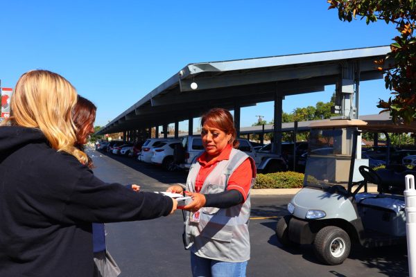 SAFETY FIRST:  School Safety Guard Luz Sanchez is seen checking students’ off campus passes on Oct. 22. During school hours, Mater Dei staff remain outside school gates to ensure only students with the proper permissions are leaving campus. “Mater Dei would be so chaotic without the security guards,” sophomore Rose Brown said. “They keep things running smoothly.”