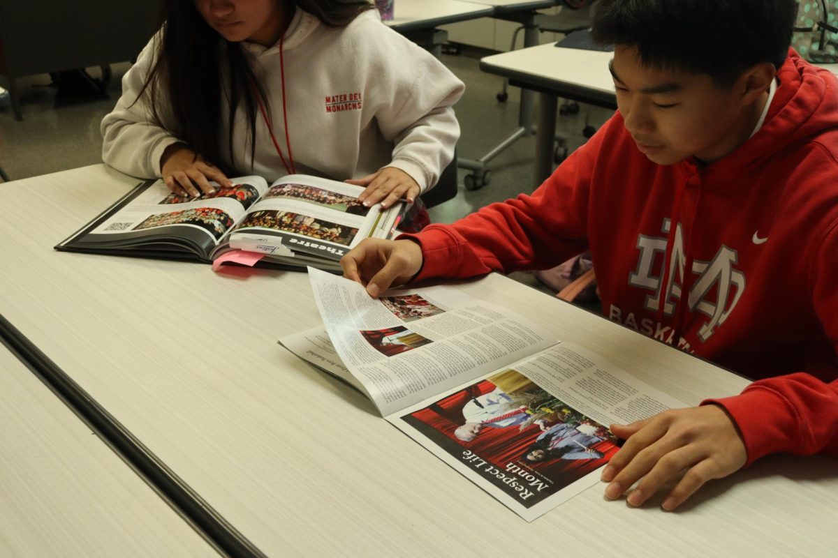 STUDENTS IN JOURNALISM Senior Ava Gomez and junior Leo Tordera read over the Mater Dei student-led publications: The CROWN Yearbook and The Scarlet Scroll Newspaper. Reviewing previous publications allows students to get a head start, learning journalistic skills, such as writing and conducting interviews, that can carry them through their professional careers. The compilation includes stories that represent both the student body as a whole, as well as highlighting world events that have an impact on the Monarch community. “Telling stories is important,” senior Sam De Guzman said. “The Scarlet Scroll has opened the world of journalism up to me.” Photo taken by Sam De Guzman. 
