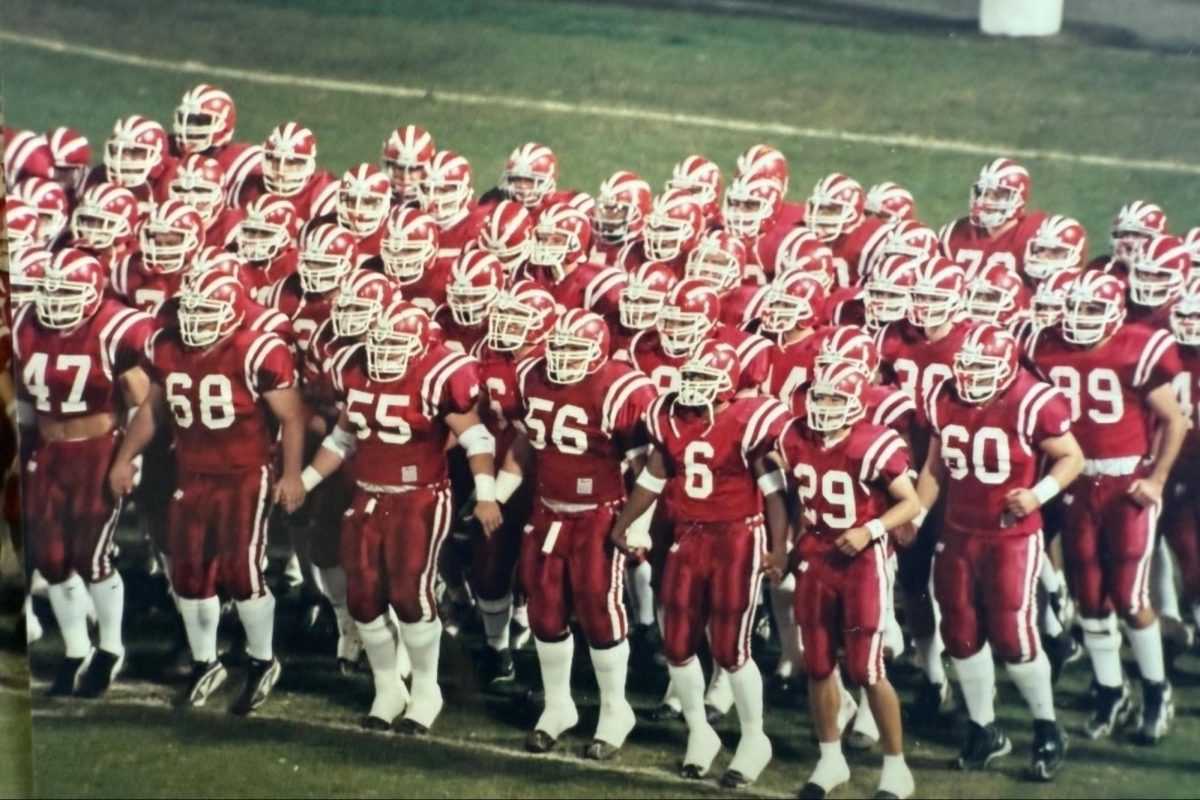 Friday Night Lights: A sea of red and white surges forward as Mater Dei football players charge onto the field before kickoff in the late 1990s. The tightly packed formation shows the unity that defined the Monarchs during an era that helped cement the program's reputation for discipline and championship ambition.